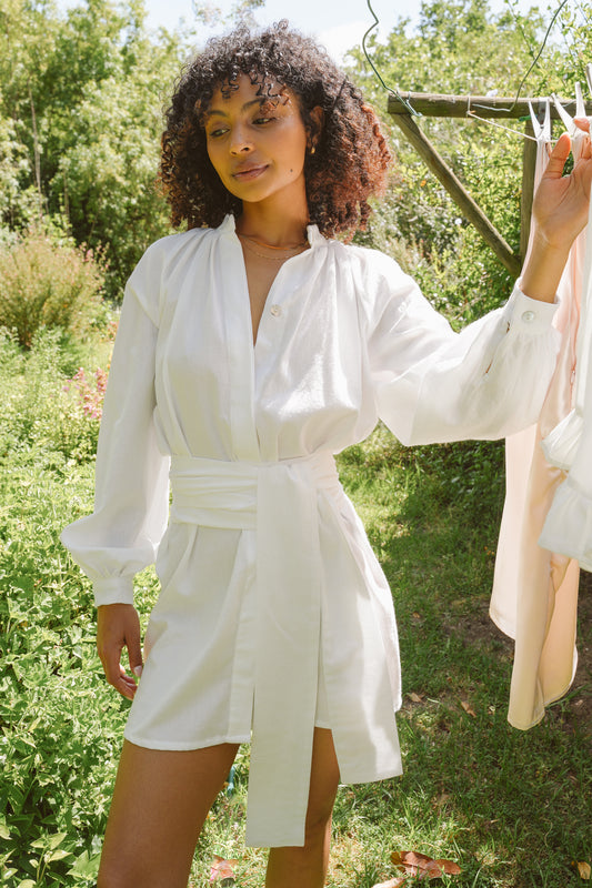 Woman wearing a white dress standing outdoors with greenery in the background