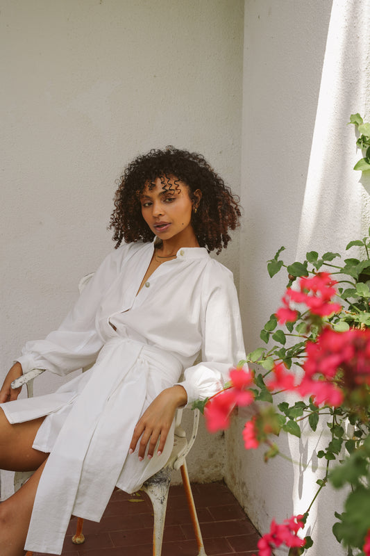 Woman in a white dress sitting on a chair with flowers in the foreground
