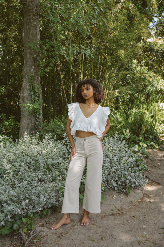 Woman in a white frilly top and oatmeal linen cotton pants standing in a garden.