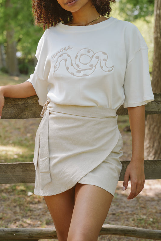 Woman leaving against a fence in a field wearing a cotton linen skirt and t-shirt