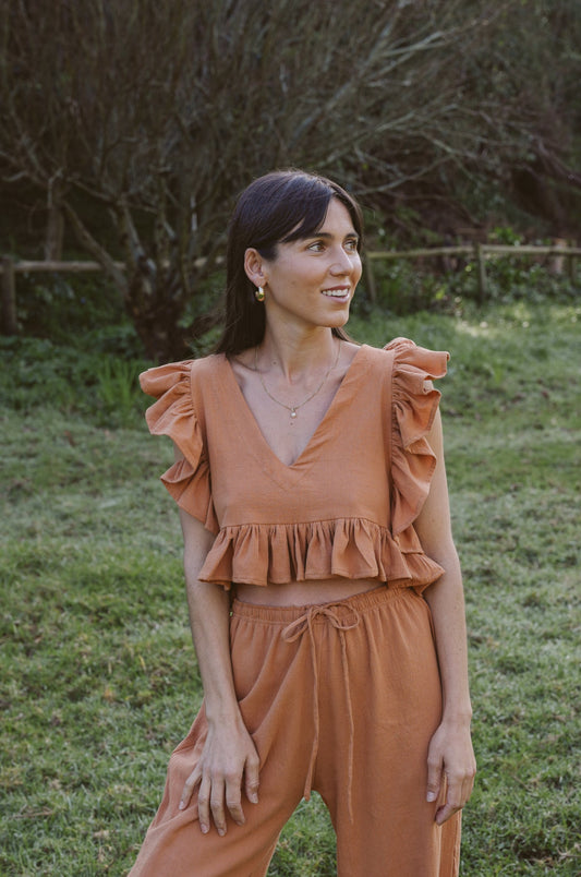Woman wearing a clay colored outfit standing in a grassy field with trees in the background
