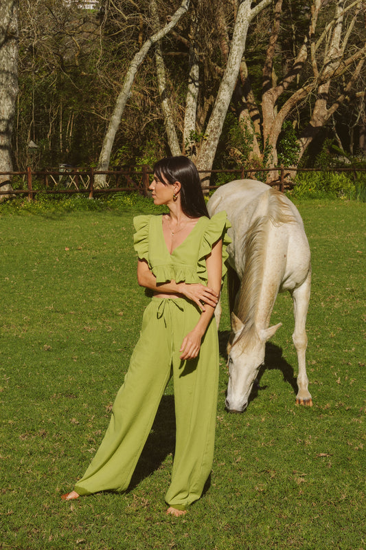 Woman in a green outfit standing next to a white horse in a grassy field with trees in the background