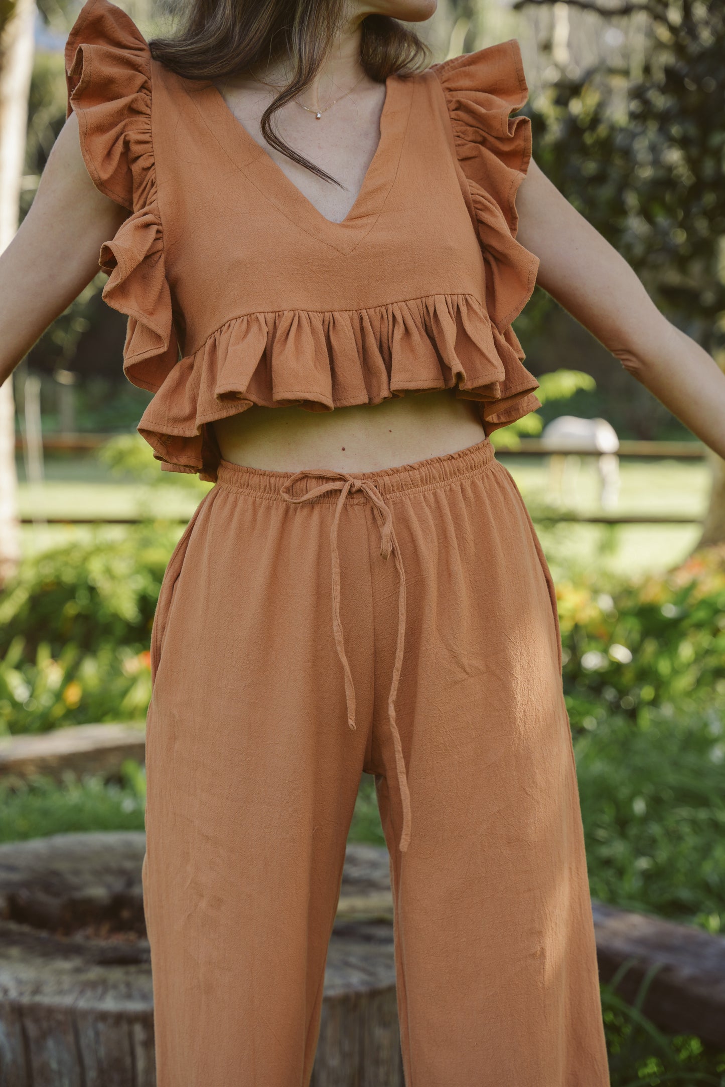 Person wearing a clay ruffled top and drawstring pants in an outdoor setting