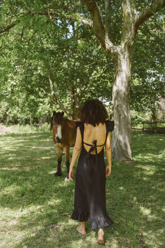 Woman in a black Poppy dress walking towards a horse in a forested area