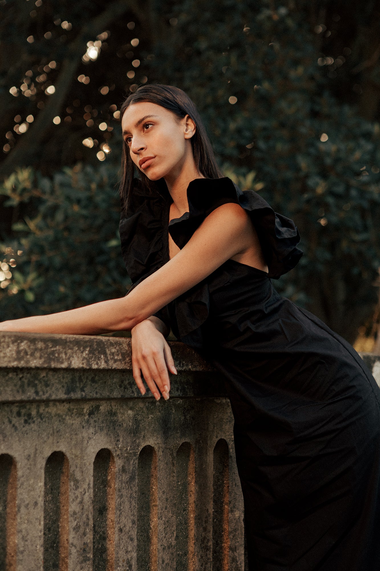 Model wearing a black Museā Poppy Dress that is maxi length. Model is posing on a bridge in the forest.
