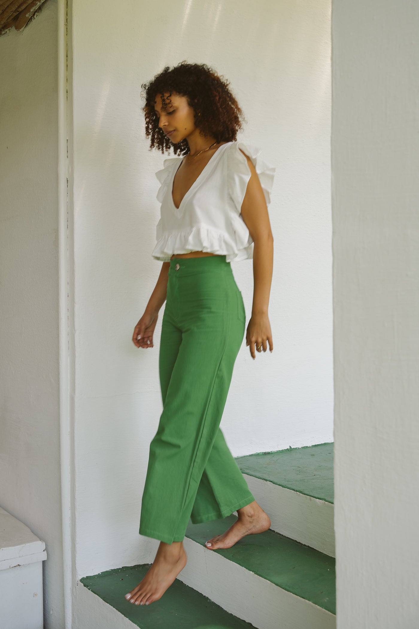 Woman wearing a white frilly top and jade green cotton pants walking down stairs