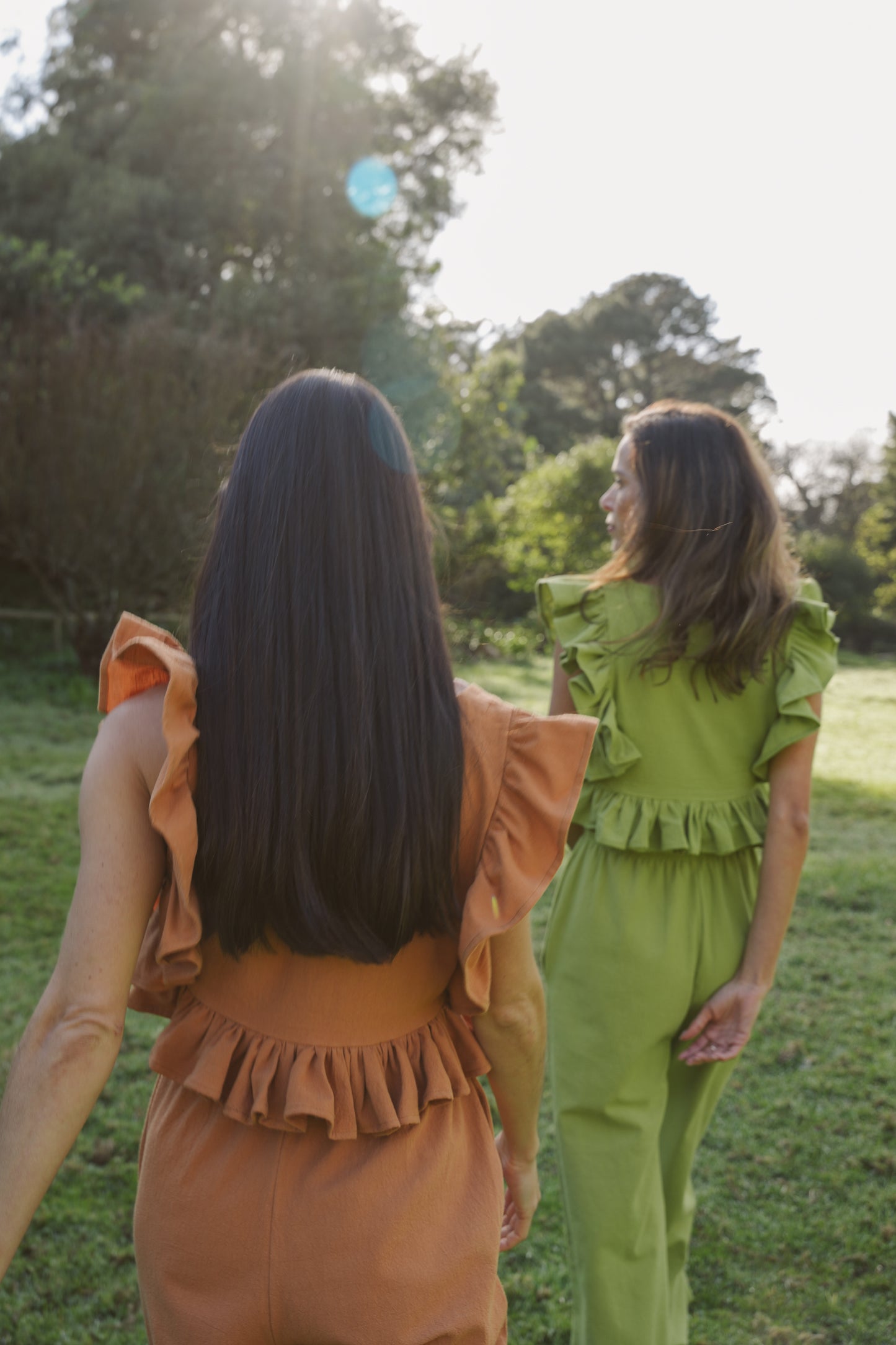 Two women in matching outfits standing in a grassy field with trees in the background.