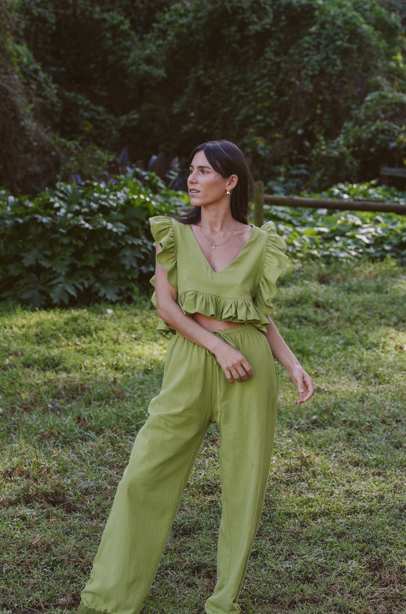 Woman in a Wasabi green outfit standing in a grassy area with trees in the background