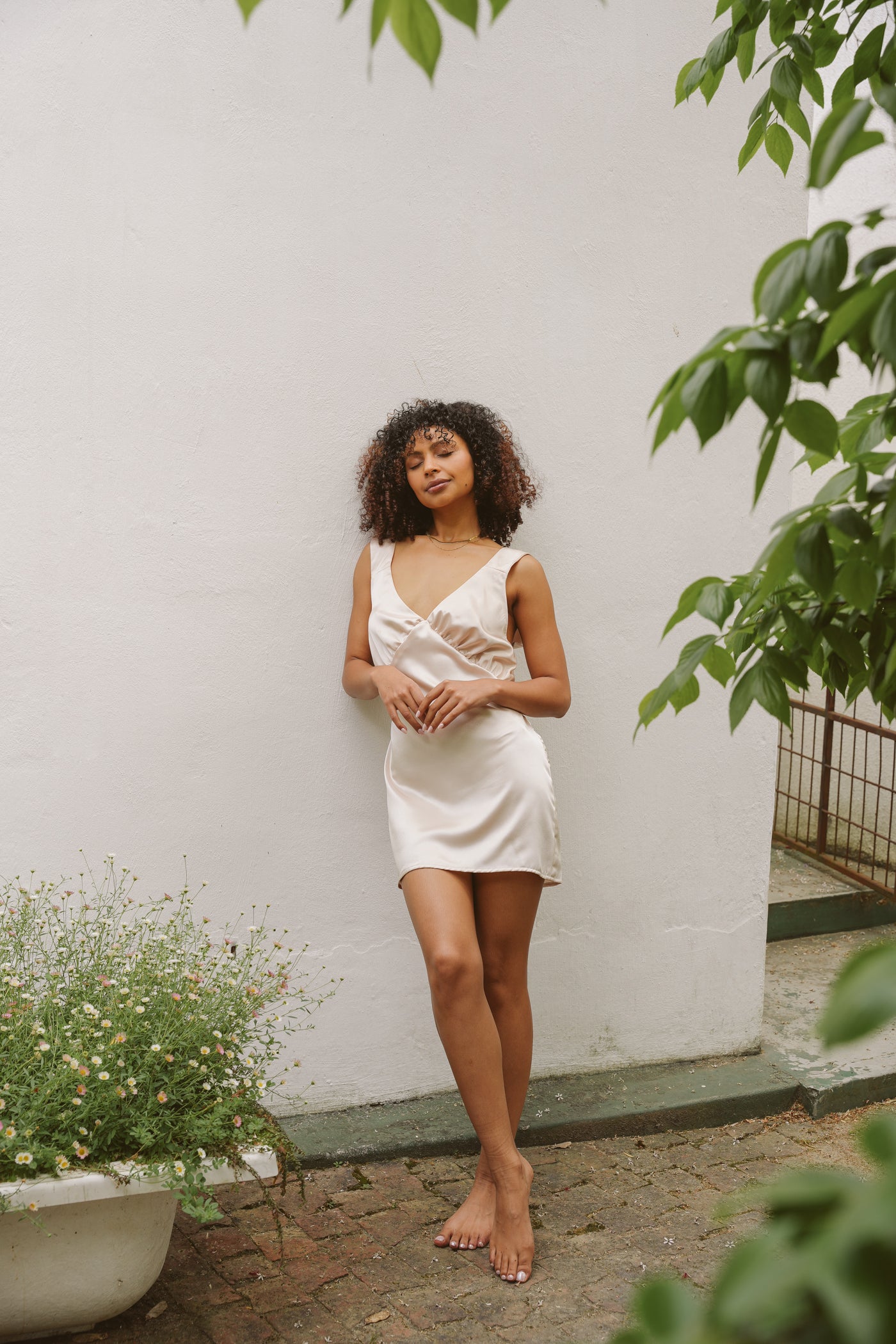 Model poses outside a house wearing satin Museā slip dress.