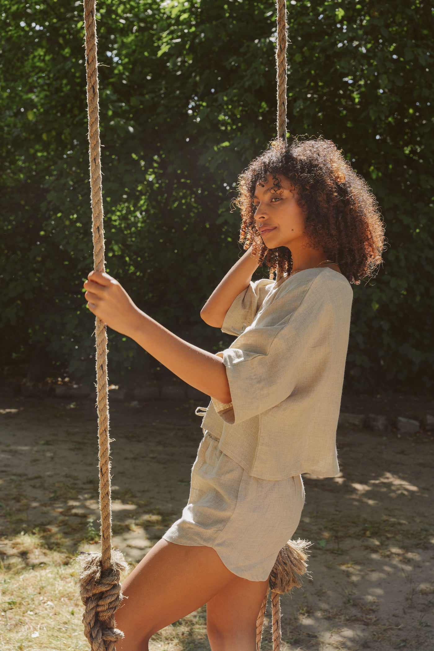 Woman in oatmeal outfit standing on a swing with trees in the background