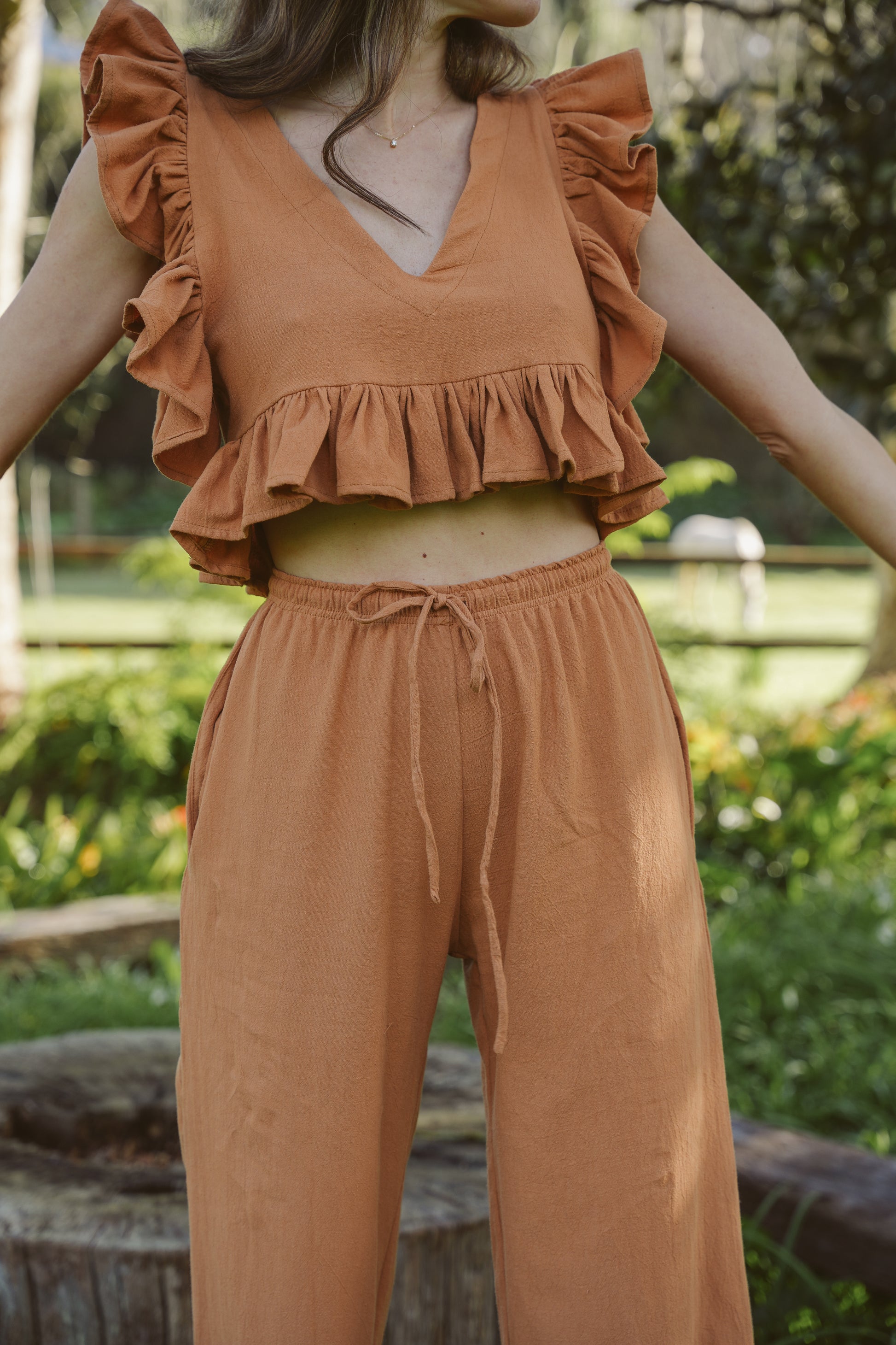 Person wearing a clay ruffled top and drawstring pants in an outdoor setting