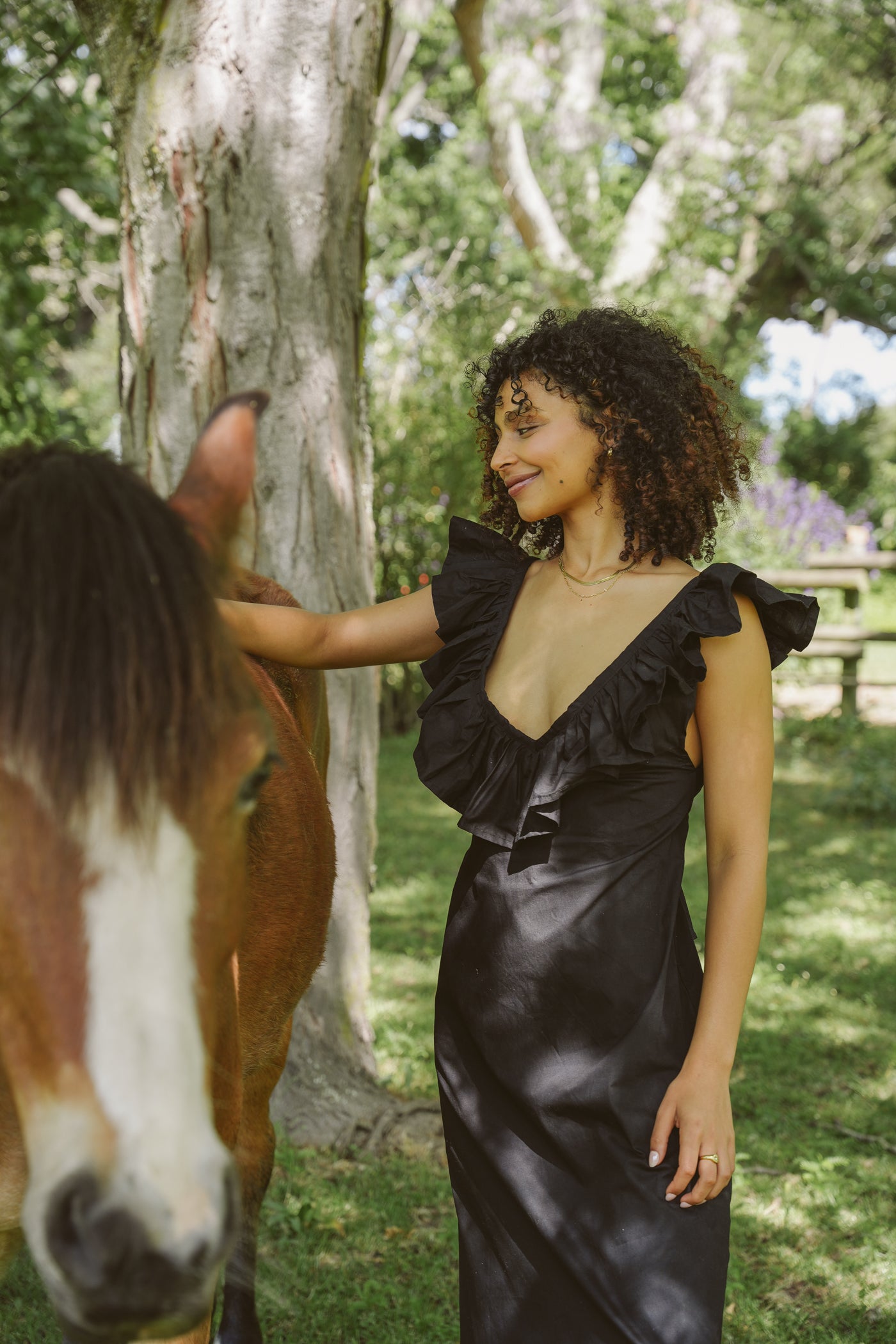 Woman in a black Poppy dress standing next to a horse in a natural setting