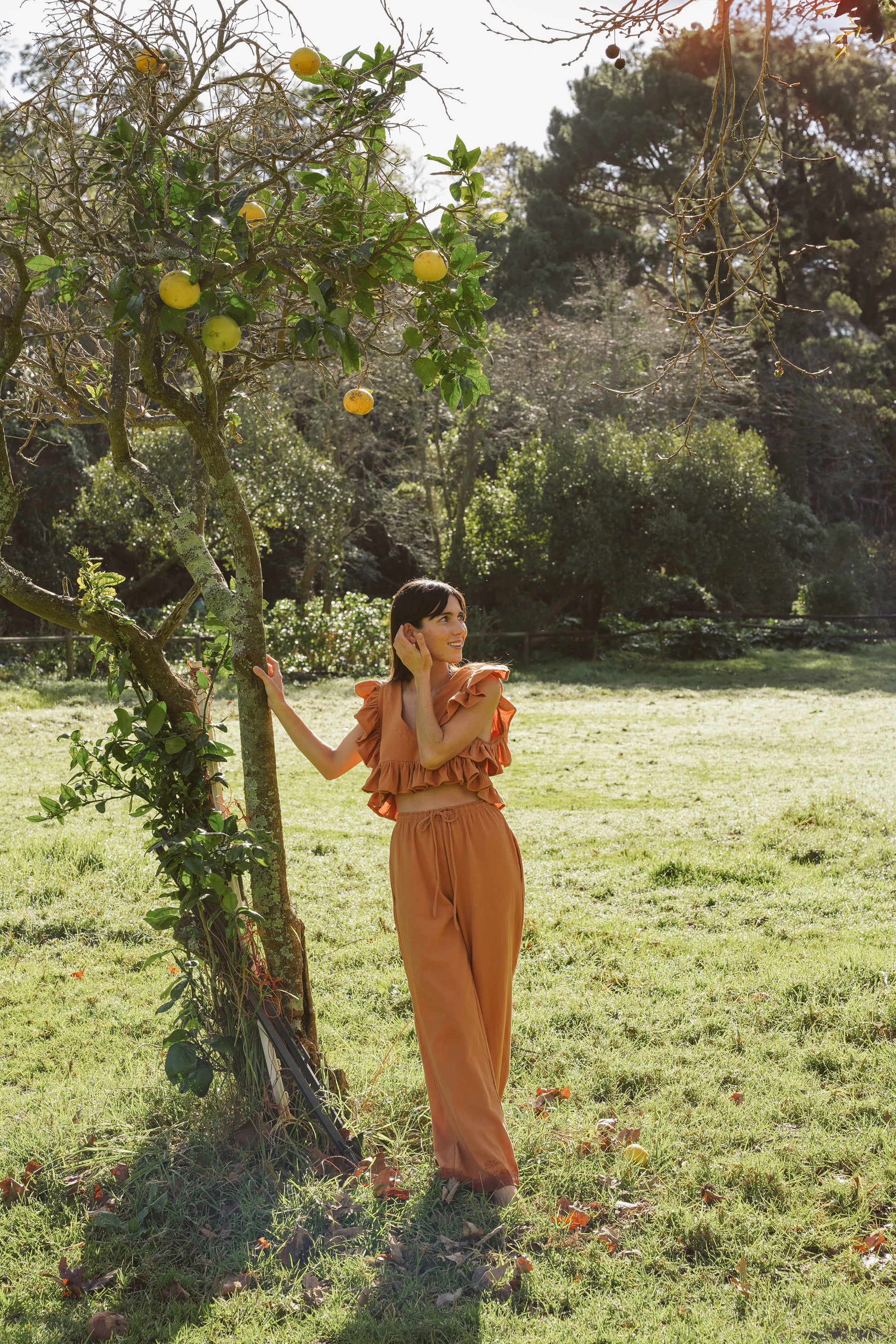Woman in an clay outfit standing next to a tree with fruit in a grassy field